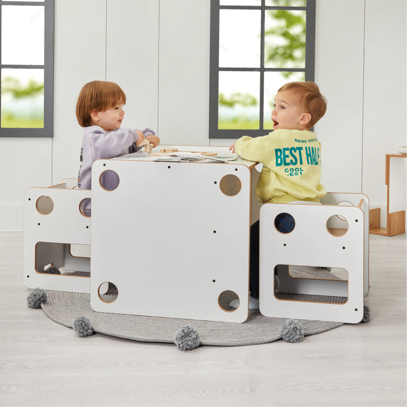 Two children playing at a white play table with circular cutouts in a bright room.